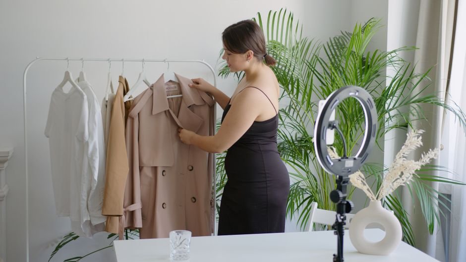 Woman in black dress arranging clothes on a rack for online selling with ring light.
