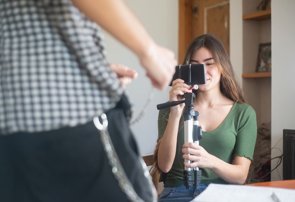 A young woman vlogs indoors using a smartphone mounted on a tripod, capturing content creation.