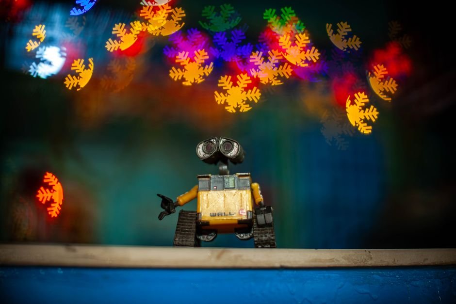Toy robot capturing colorful bokeh lights in a vibrant, festive indoor setting.